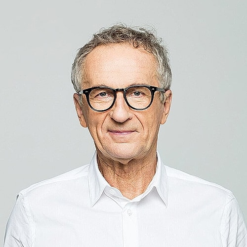 Smiling older man in glasses, white shirt.